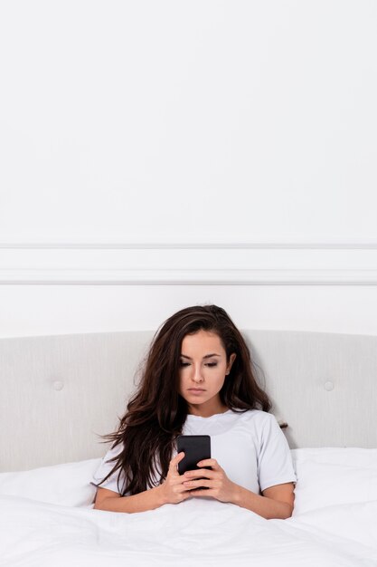 Free photo young woman checking her phone in bed