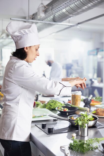 Young woman chef in restaurant kitchen carefully sprinkles fresh herbs