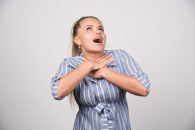 Free photo young woman choking herself on gray wall.