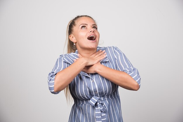 Young woman choking herself on gray wall.