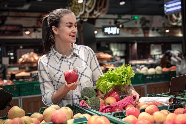 젊은 여성이 슈퍼마켓에서 과일과 채소를 선택합니다