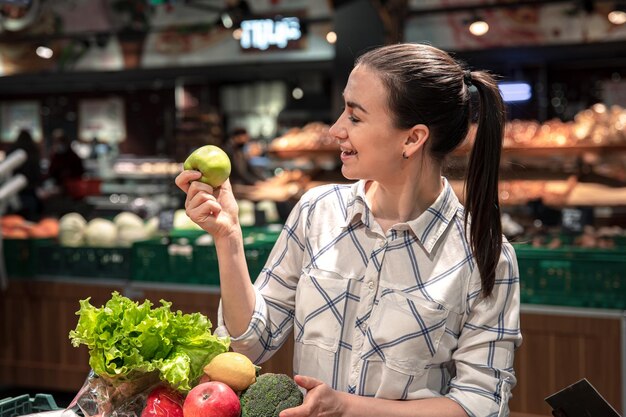 若い女性がスーパーマーケットで果物や野菜を選ぶ
