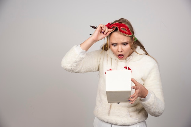 Young woman in christmas sweatshirt looking at gift box excitedly.