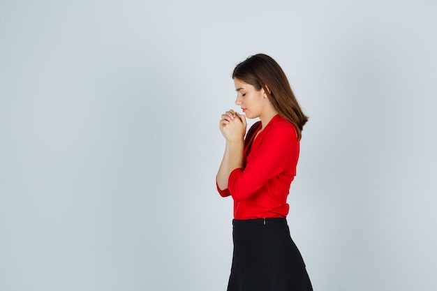 Young woman clasping hands in praying position in red blouse