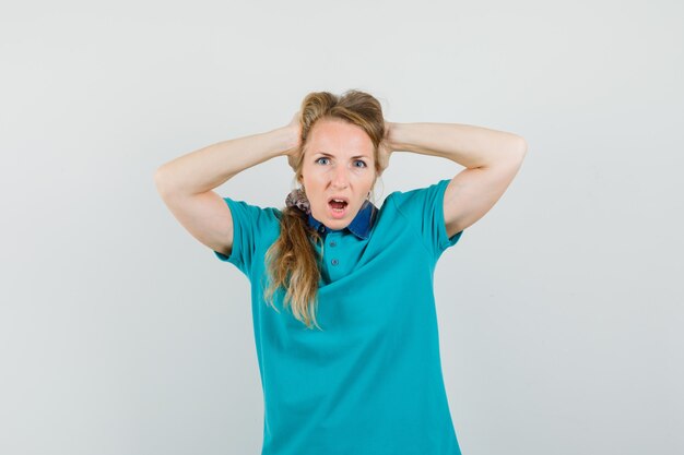 Young woman clasping head with hands in t-shirt and looking irritated 