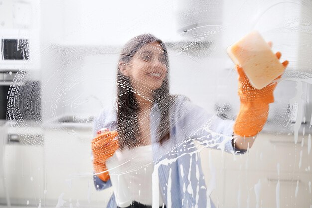 Young woman cleaning dirty window with special detergent