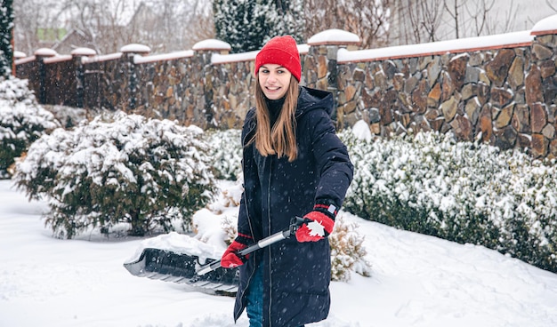 若い女性は雪の天気で庭の雪をきれいにします