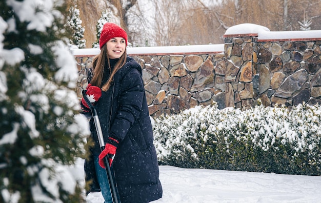 若い女性は雪の天気で庭の雪をきれいにします