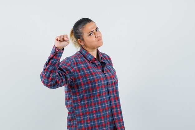 Young woman clenching fist in checked shirt and looking serious , front view.