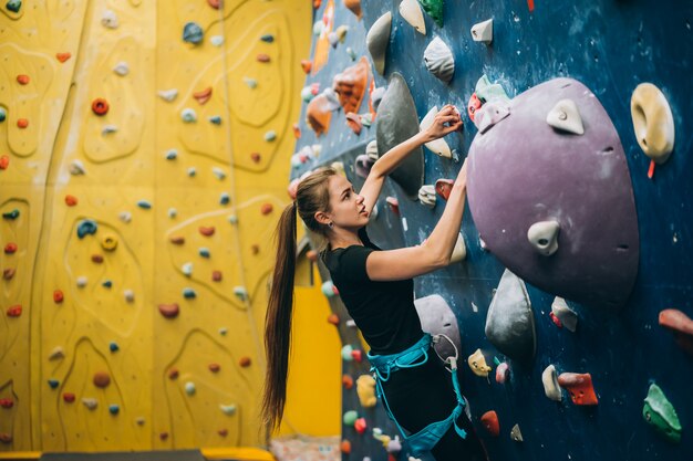 Young woman climbing a tall, indoor, man-made rock climbing wall