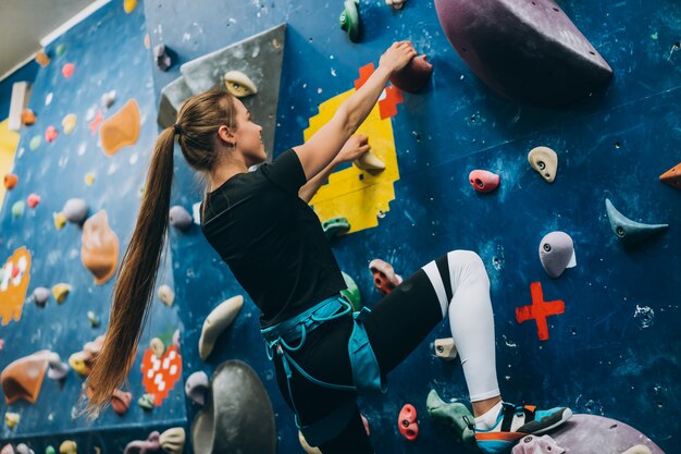 Young woman climbing a tall, indoor, man-made rock climbing wall