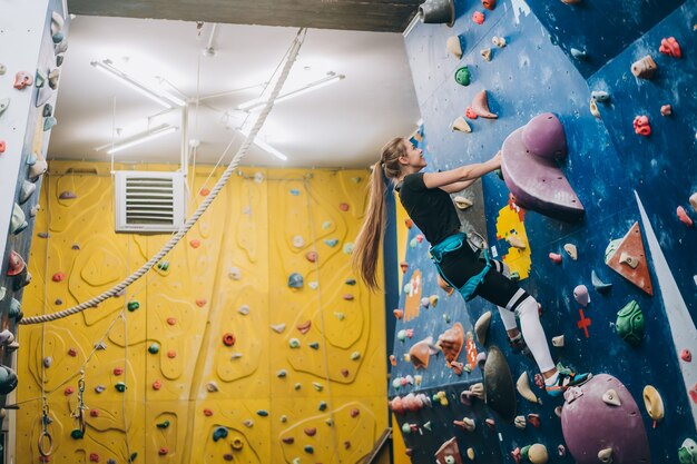 Young woman climbing a tall, indoor, man-made rock climbing wall