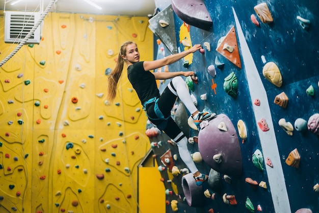 Foto gratuita giovane donna che scala una parete di arrampicata su roccia alta, indoor, artificiale