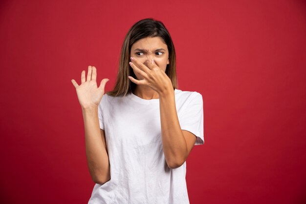 Young woman closing her nose on red wall. 