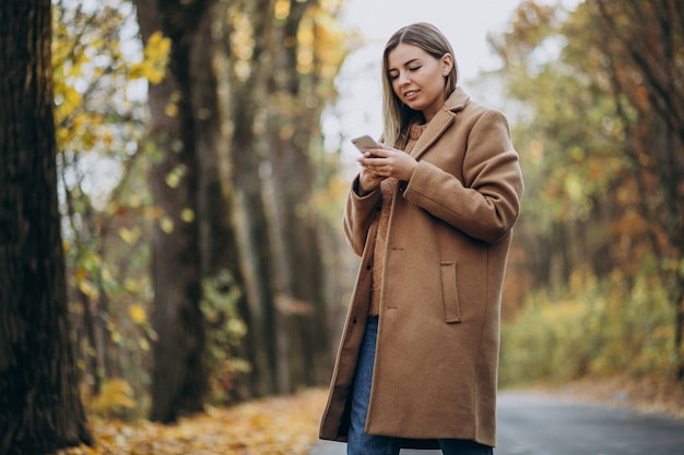 Молодая женщина в пальто стоя на дороге в парке осени
