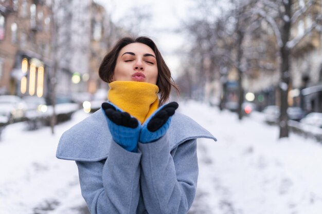 A young woman in a coat and a yellow scarf on the city boulevard in the evening smiles cheerfully