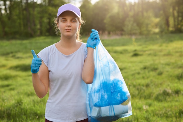 Young woman collects garbage out from grasses in garden