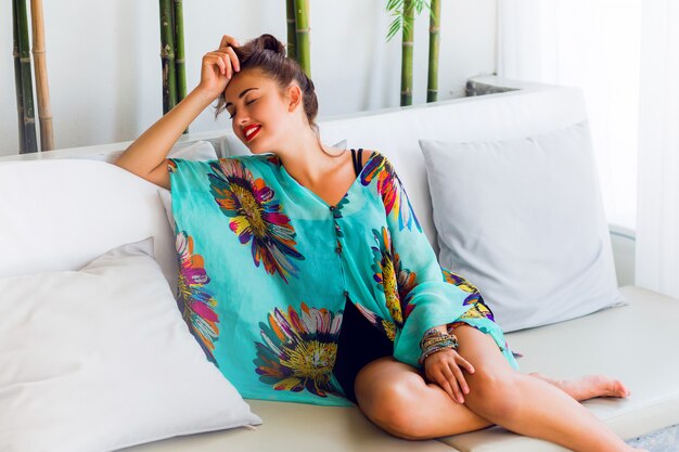 Young woman in colorful boho outfit relaxing on white sofa