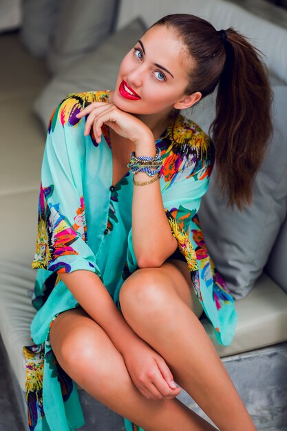 Young woman in colorful boho outfit relaxing on white sofa