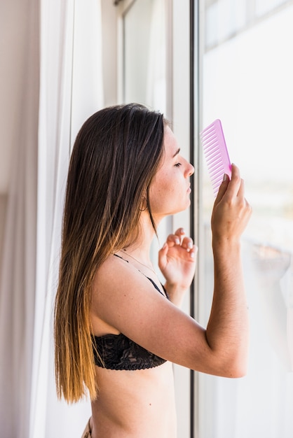 Young woman combing her hair near the window