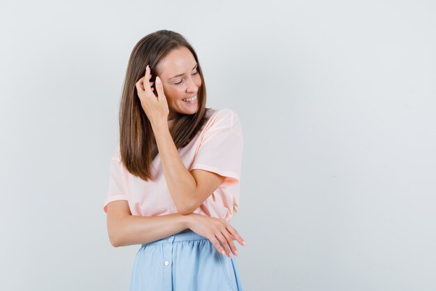 Young woman combing her hair with fingers in t-shirt, skirt and looking happy. front view.