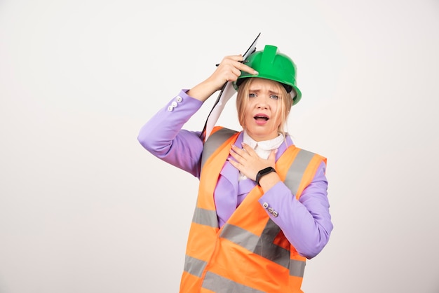 Young woman contractor with green helmet and clipboard on white.