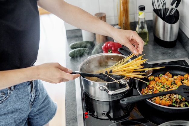 野菜と一緒に家で新鮮なスパゲッティパスタを調理する若い女性。