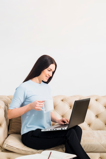 Foto gratuita giovane donna sul divano con caffè e laptop