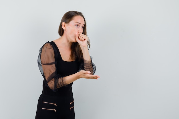 Young woman coughing while talking with someone in black blouse and looking sick. front view. space for text