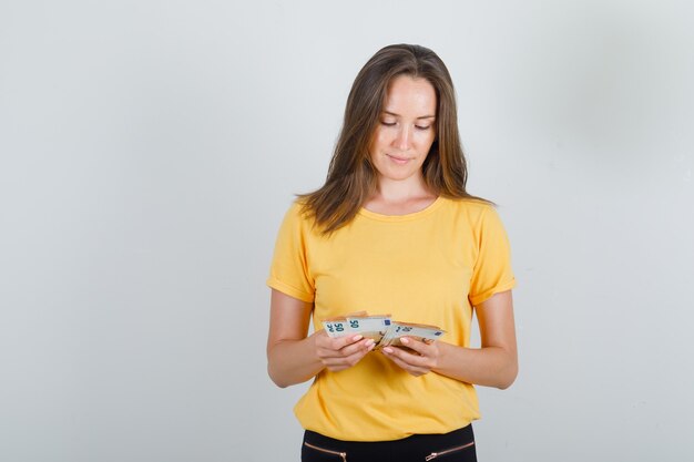 Молодая женщина считает деньги в желтой футболке, черных штанах и внимательно смотрит