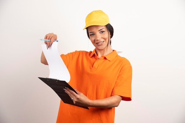 Young woman courier holding clipboard on white wall.