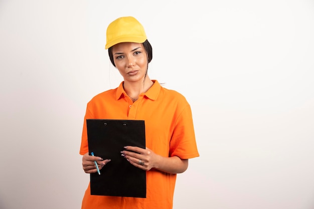 Young woman courier holding clipboard on white wall.