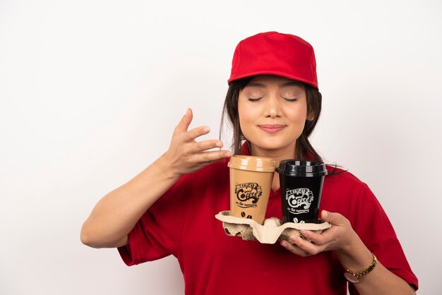 Free photo young woman courier sniffs aroma coffee for delivery on white background