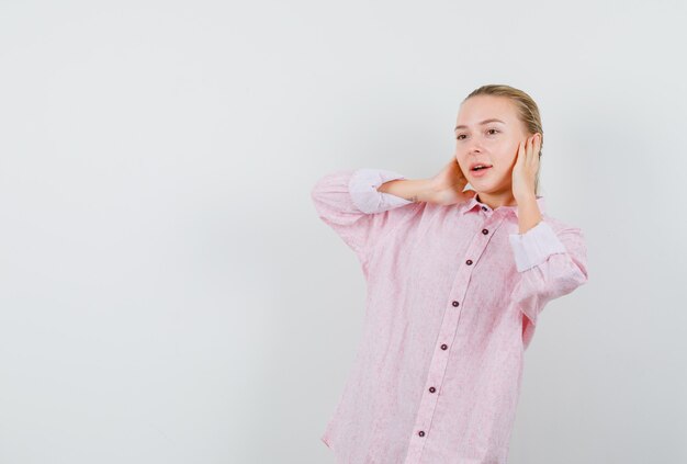 Giovane donna che copre le orecchie con le mani in camicia rosa e guardando positivo