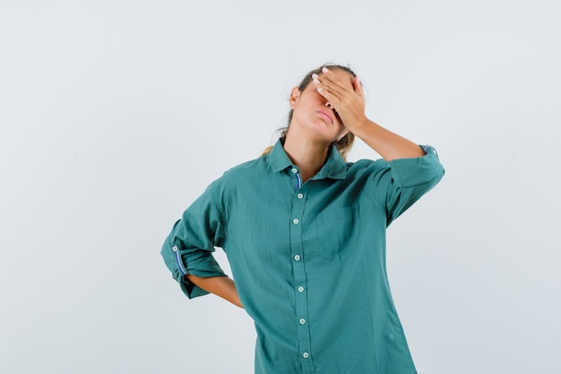 Young woman covering eyes with hand in green blouse and looking tired