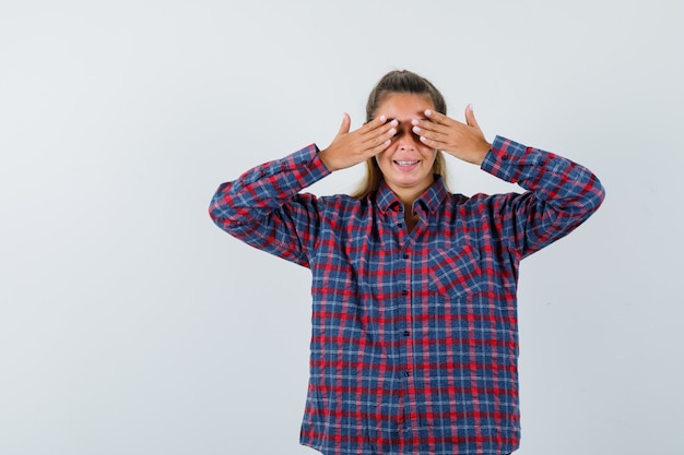 Young woman covering eyes with hands in checked shirt and looking pretty