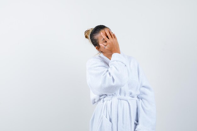 Young woman covering face with hand in bathrobe and looking forgetful