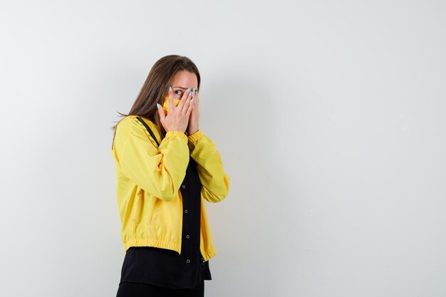 Young woman covering face with hand and looking scared