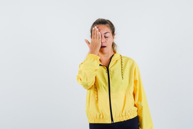 Young woman covering face with hand in yellow raincoat and looking calm