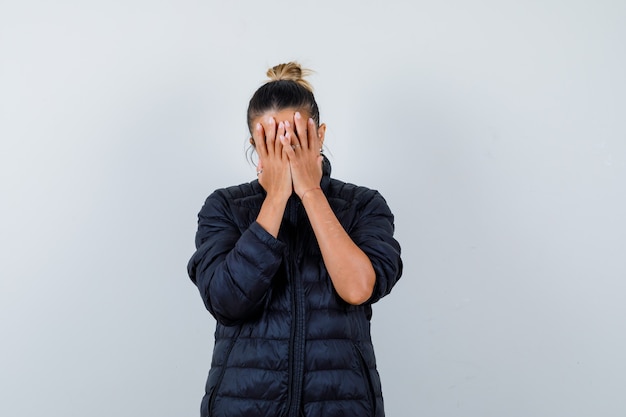 Young woman covering face with hands in puffer jacket and looking depressed. front view.