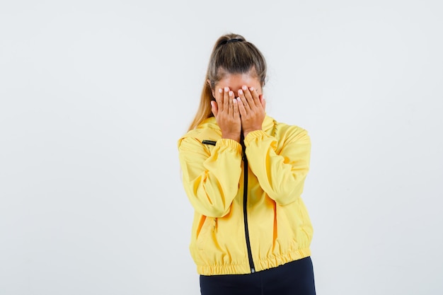 Young woman covering face with hands in yellow raincoat and looking sorrowful