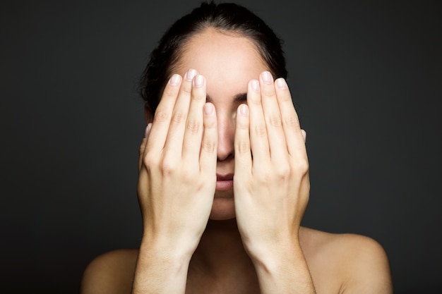 Giovane donna che copre metà del suo volto con una mano.