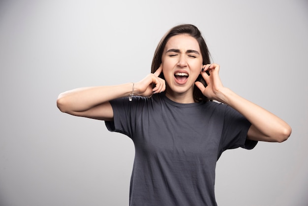 Young woman covering her ears over a gray background .