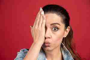 Free photo young woman covering her eye by hand on a red background. high quality photo