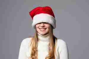 Foto gratuita giovane donna che si copre gli occhi con il cappello di babbo natale isolato sul muro grigio