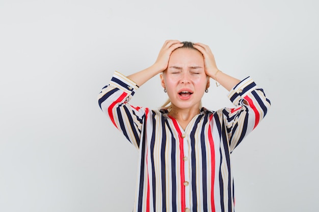 Free photo young woman covering her head with hands and trying to scream in striped blouse and looking exhausted