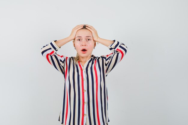 Young woman covering her head with her hands in striped blouse and looking shocked