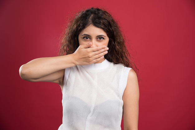 Free photo young woman covering her mouth on a red.