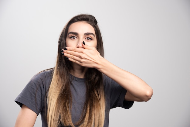 Young woman covering her mouth with hand over a gray background.