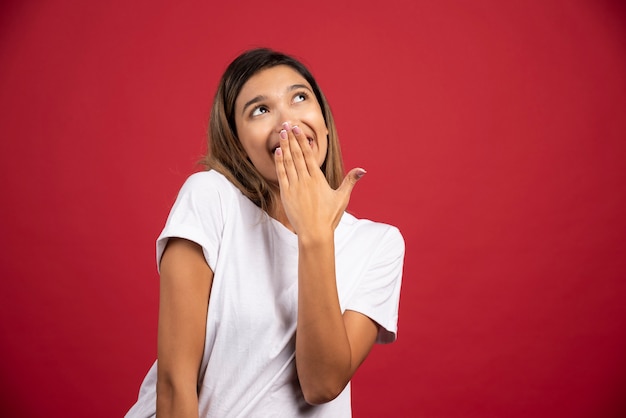 Young woman covering her mouth with hand on red wall. 